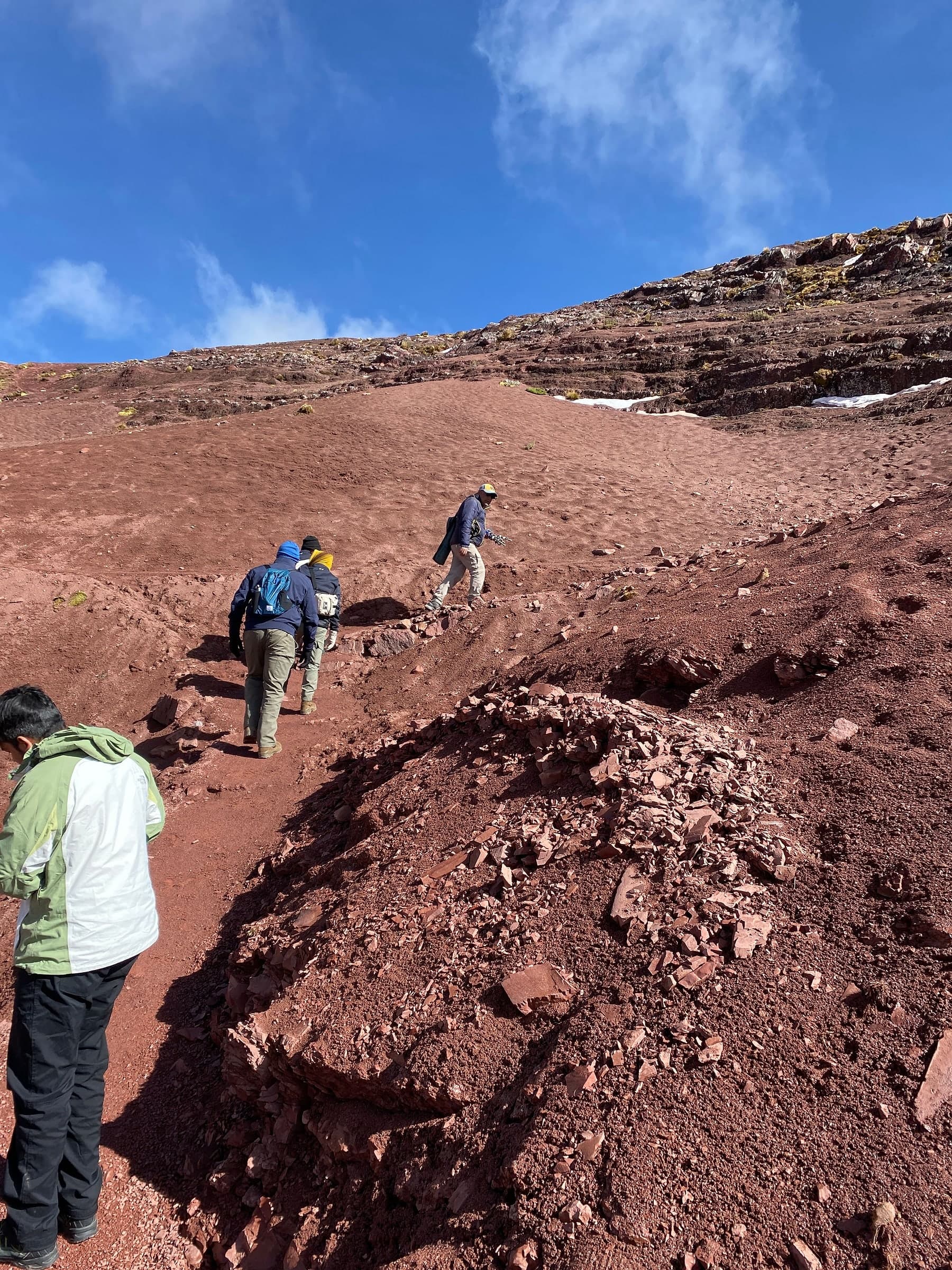 Hikers climbing the steep red trail towards the Rainbow Mountain viewpoint